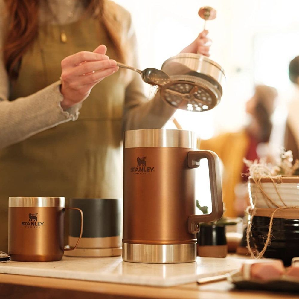 Women spooning in coffee grounds into a copper stanley french press.