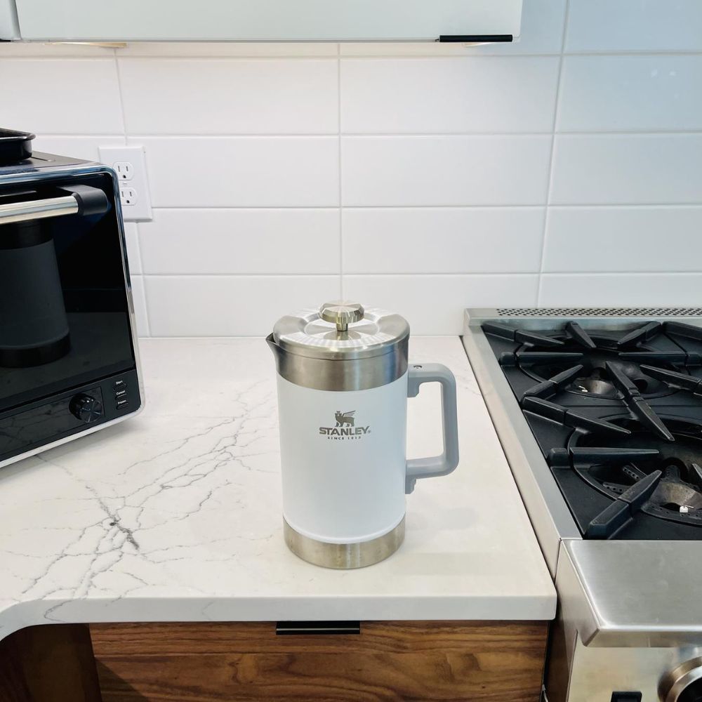 Stanley French Press sitting on a marble counter between a microwave and gas stove.