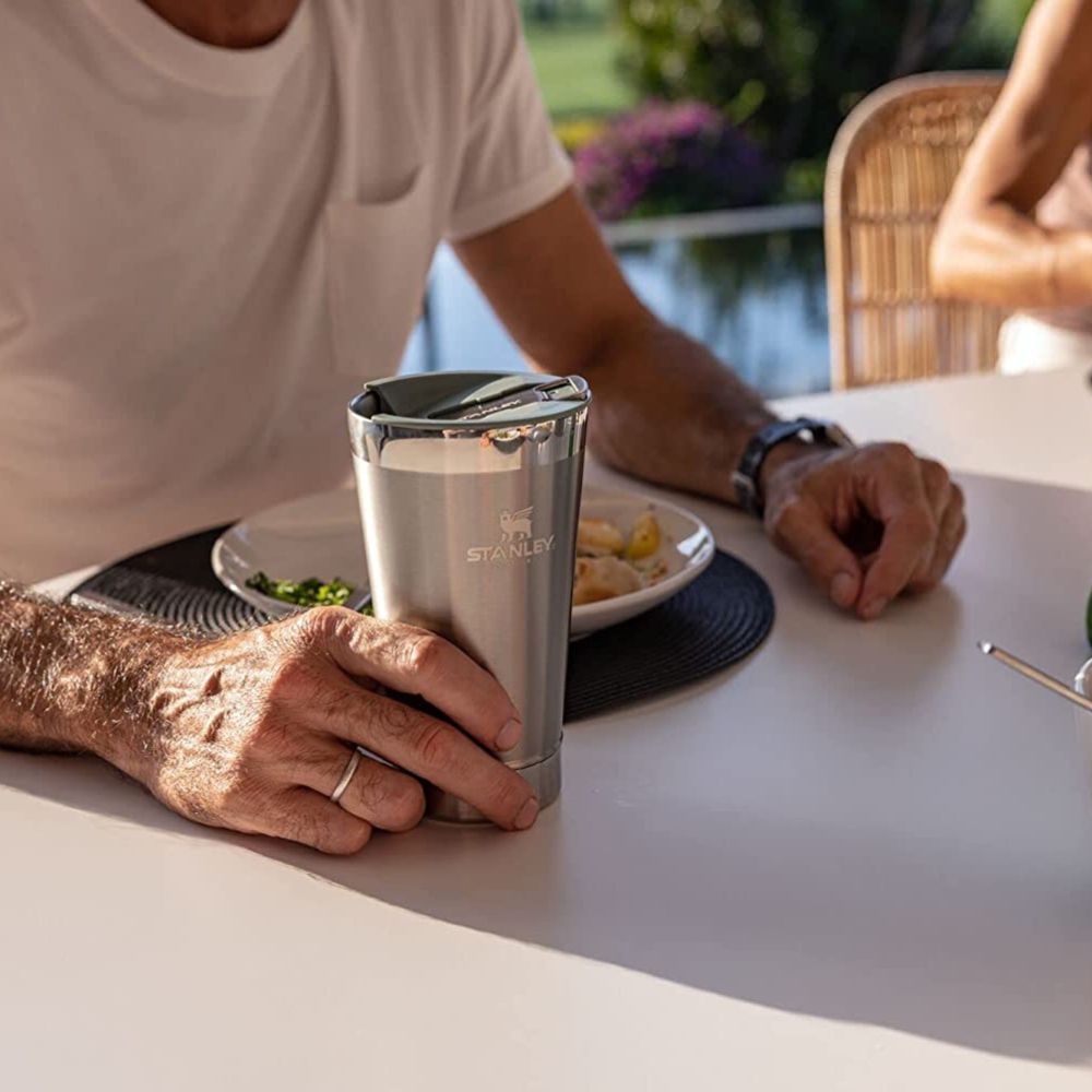 Man sitting at an oudoor dinner table with a plate of food and a Stanley stainless steel beer pint.