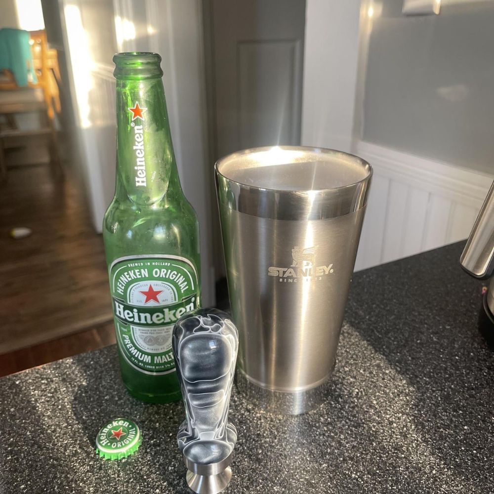 Open Heineken beer bottle next to a Stanley stainless steel classic stay chill beer pint.